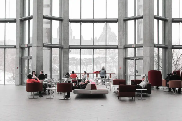 A spacious, modern lobby with large windows, visitors relax on couches while enjoying views of a snowy landscape outside.