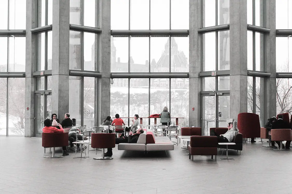 A spacious, modern lobby with large windows, visitors relax on couches while enjoying views of a snowy landscape outside.